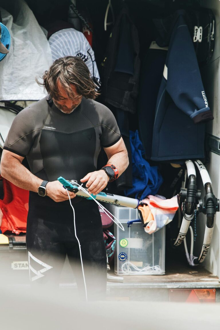 A man wearing a wetsuit prepares diving equipment near a vehicle.