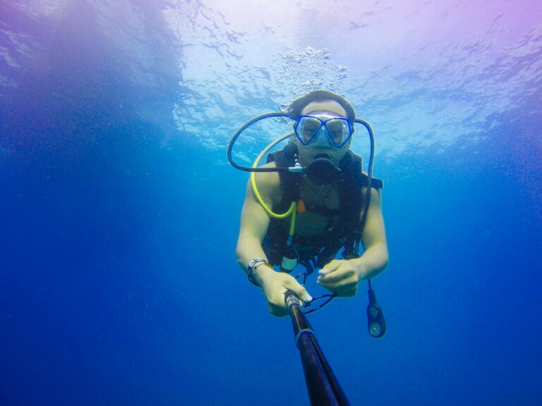 A scuba diver explores the vibrant underwater world in Thailand, capturing the moment with a monopod.